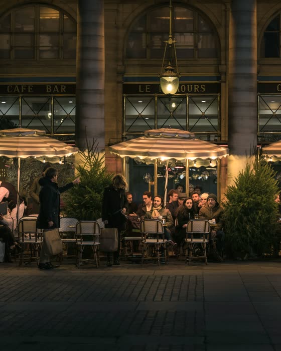 A brasserie terrace at night, full, under lit umbrellas.