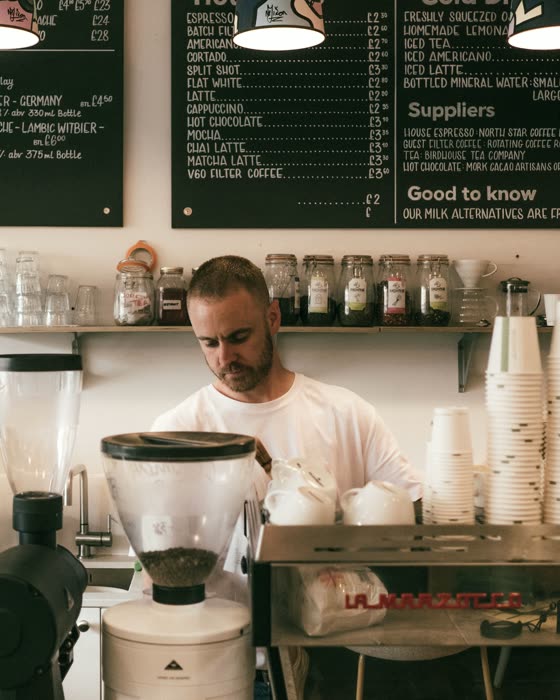 A barista working an espresso bar beneath handwritten menu boards.